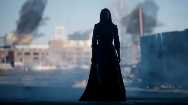 A silhouetted woman in a dress against a burning city